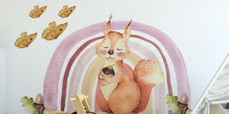 Nursery wall sticker featuring a cute squirrel holding a baby in front of a pastel rainbow, with small flying leaves above.