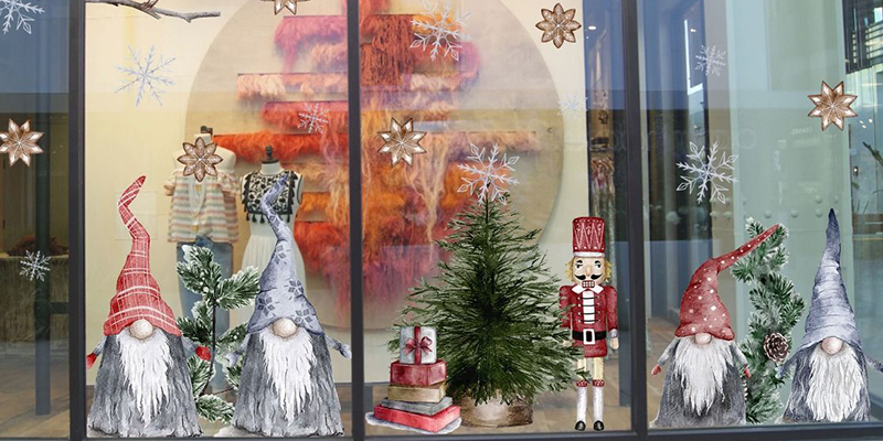 Holiday window display featuring gnome figurines, a nutcracker, small pine trees, and snowflake decorations for a festive look.