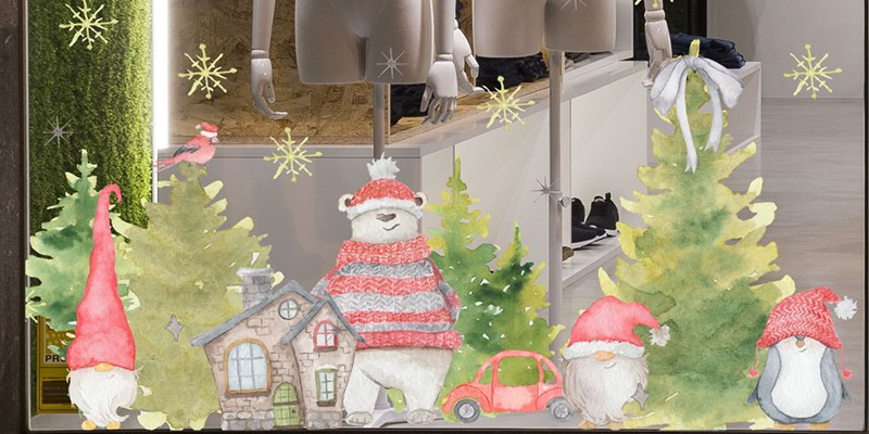 Festive window display with Christmas gnomes, pine trees, a cozy cottage, and snowflake decals for a winter holiday theme.