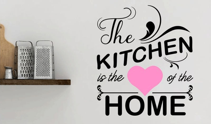 Wall sticker with the quote "The kitchen is the heart of the home" in decorative fonts, featuring a pink heart.