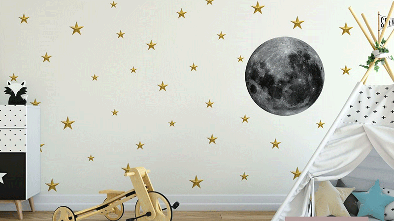 Nursery wall stickers featuring a large moon with scattered gold stars, paired with a play tent and wooden toy.
