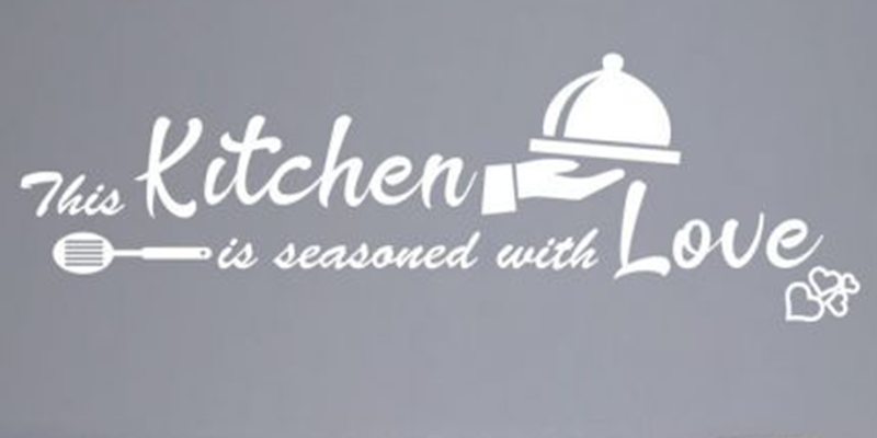 White kitchen wall decal with the phrase "This kitchen is seasoned with love," featuring a serving dish and spatula design.