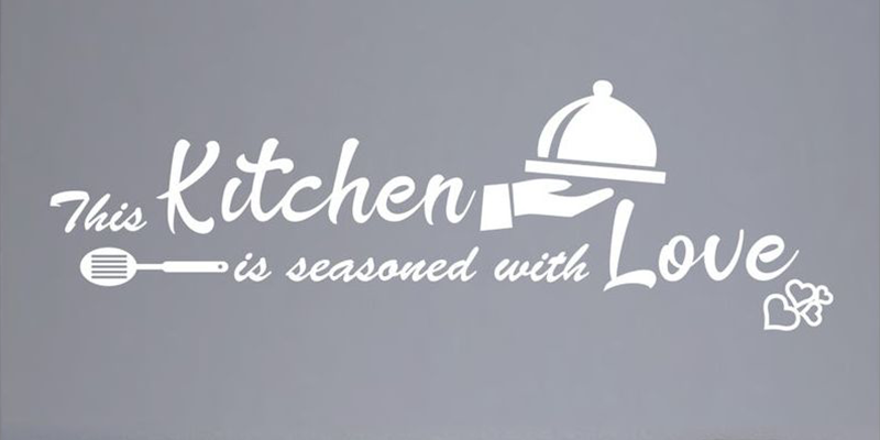 White kitchen wall decal with the phrase "This kitchen is seasoned with love," featuring a serving dish and spatula design.